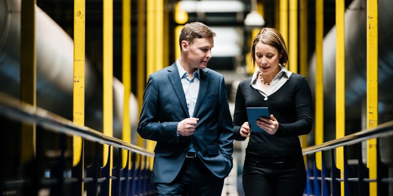 Man and woman walking in a factory while looking at a tablet