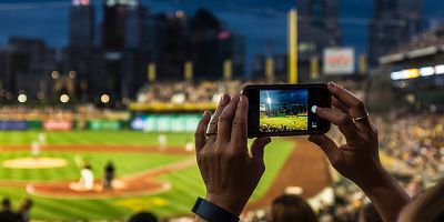 Hands holding a smartphone recording a baseball game.