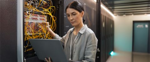 Businessperson holds laptop in one hand while wiring a server stack with the other. 