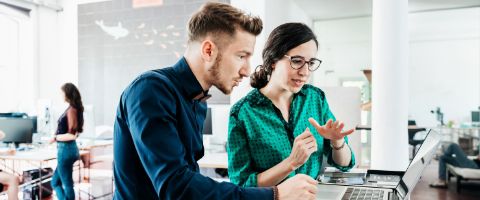 Two people work in front of a laptop in a bright office.