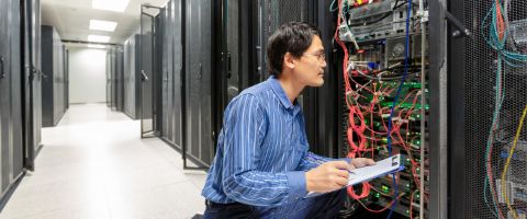 Technician inspecting network equipment and cabling in a data center server room.