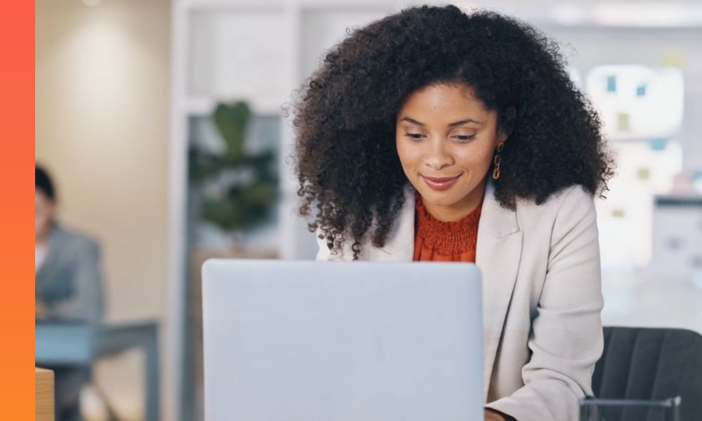 Businessperson in a blazer works from a laptop and smiles. 