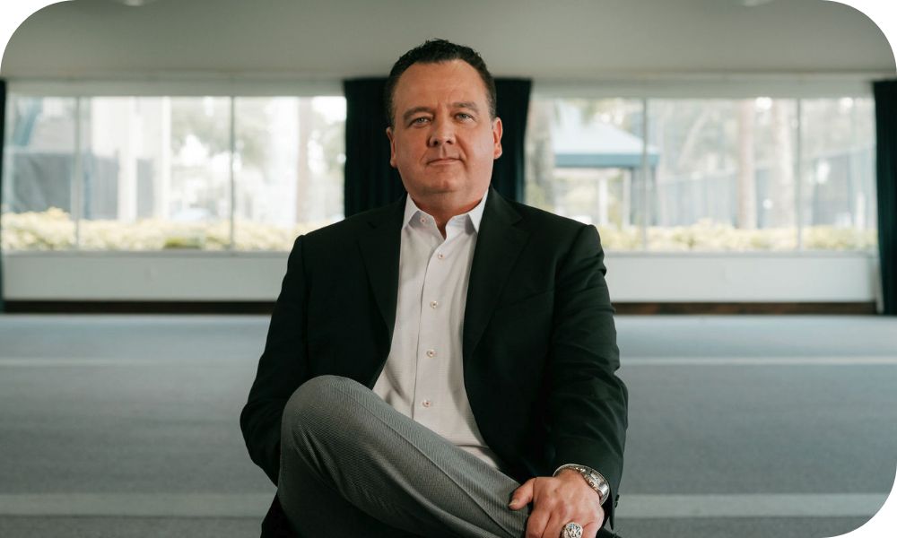  Business professional wearing a suit jacket and slacks with their leg crossed over the other and using one hand to grab onto their ankle.