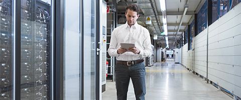 A data security professional walks around a data center looking at analytics on a tablet that he is holding 