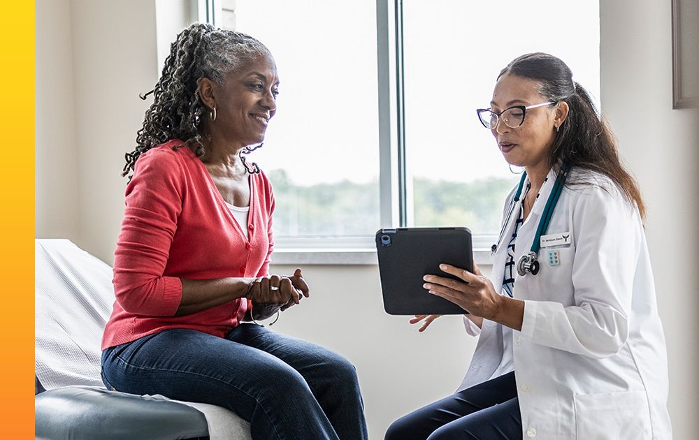 Healthcare professional in a white coat using a tablet to review information during a patient consultation, illustrating technology-enabled care.