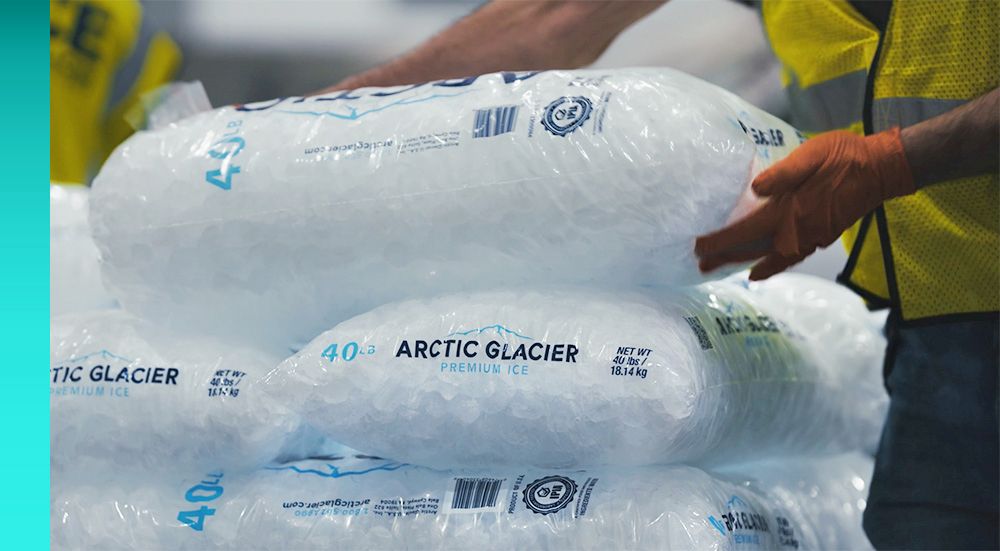 A pile of Arctic Glacier ice is handled by a worker wearing a yellow vest. 