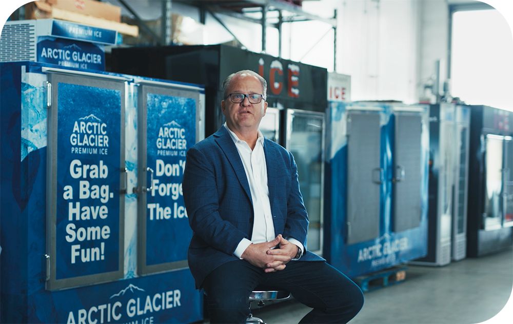 Businessperson sits in front of freezers with Arctic Glacier logo on them.