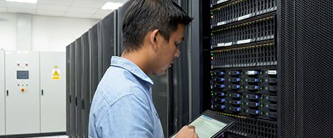 A person stands close to a server stack and works on a tablet device in a bright server room.