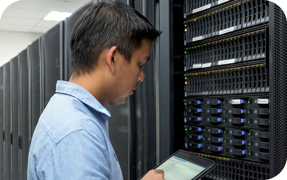 A person stands close to a server stack and works on a tablet device in a bright server room.