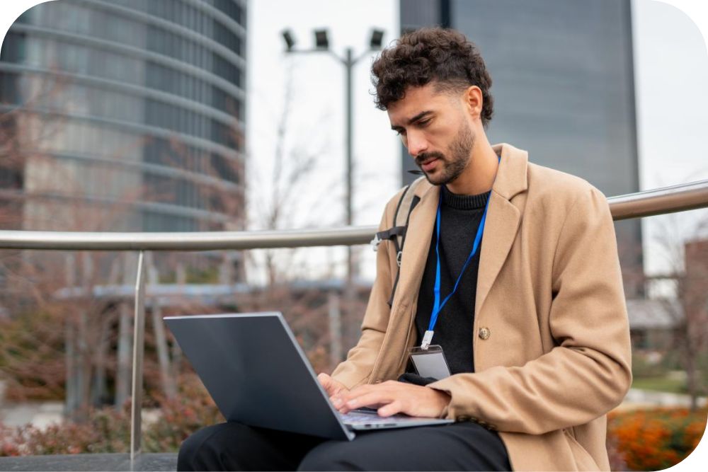 An individual sits outside and works on their laptop.
