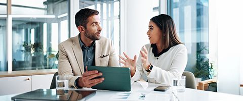 Two businesspeople have a discussion while one holds a tablet 