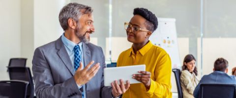 Two people hold a tablet device and have a conversation in an office.