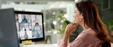 A person sits at a desk and participates in a video call on a desktop computer.