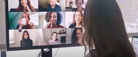 Woman looking at a monitor image of nine people on a video call 