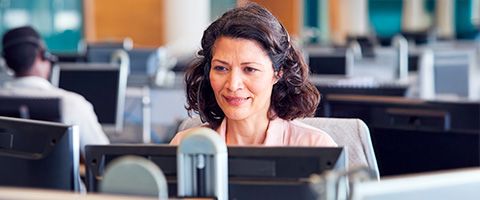 A person works at a desktop computer in an office and smiles.