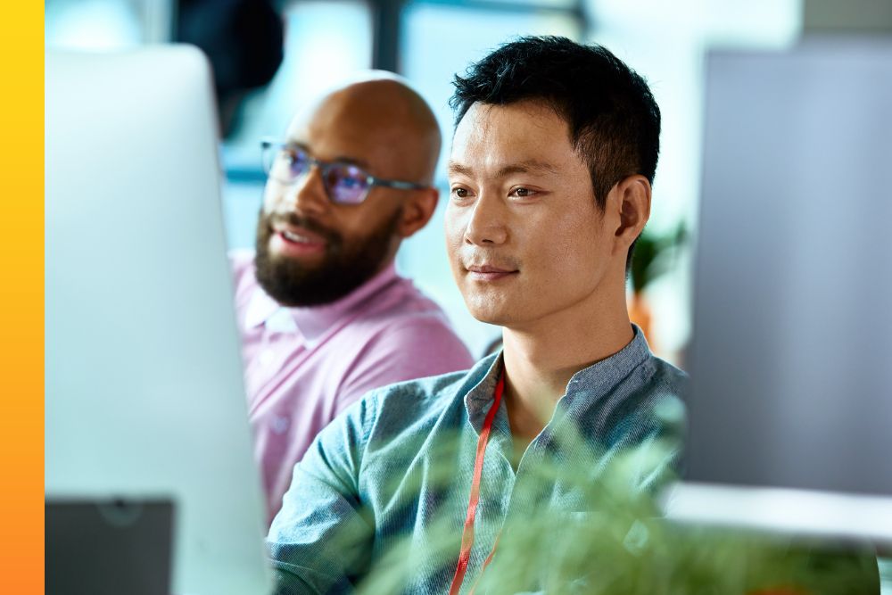 Two men sitting at a row of desks while working on desktop computers