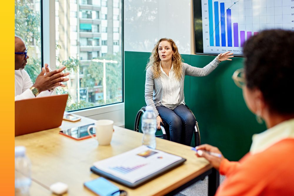 Woman sitting in a wheelchair while presenting a graph to a conference room