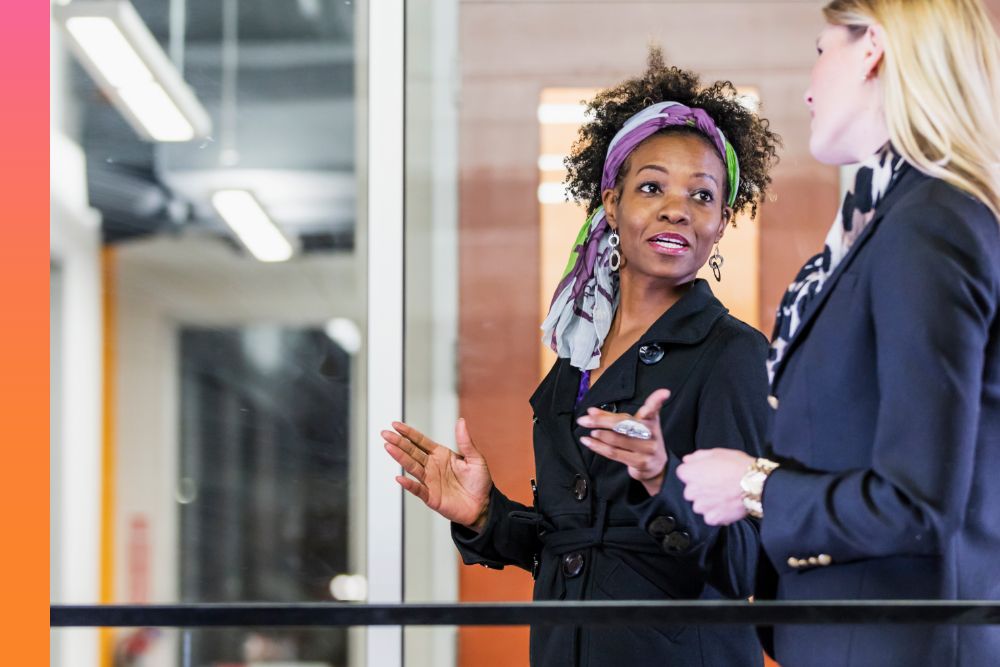 Two women in black coats standing while talking to each other