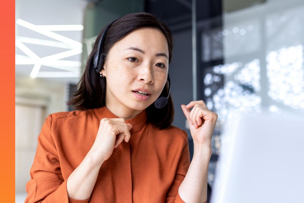 Woman in an orange shirt sitting while talking to someone on a headset