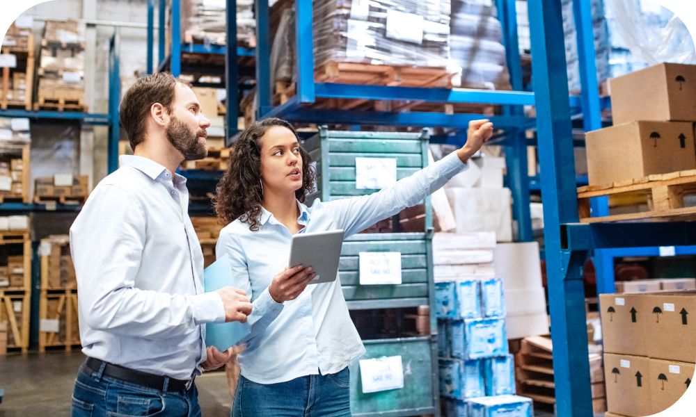 Two people in white shirts standing on a factory floor while looking at something on an iPad