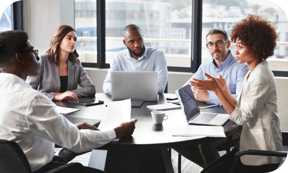 Group of five people sitting around a conference table while working on laptops