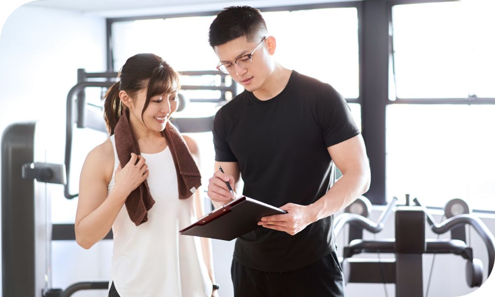 Woman in white and man wearing black standing in a gym while looking at an iPad