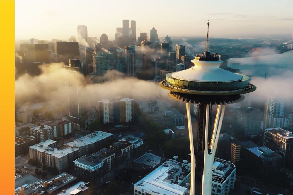 Aerial view of the Seattle Space Needle emerging above low-lying morning fog engulfing the downtown skyline at sunrise.