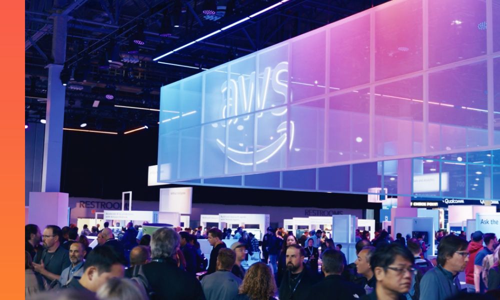 Crowded AWS re:Invent expo floor featuring illuminated AWS signage and multiple exhibition booths inside a large convention hall.
