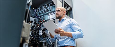 An individual in a data center holds a tablet while checking the server racks.
