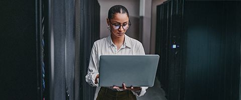 Businessperson in a server room works on a laptop