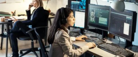 Person seated at a desk using multiple monitors in a modern office workspace.