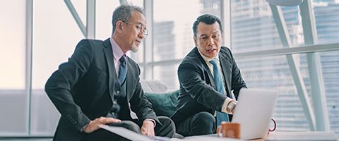 Two people in business attire talk and point at something on a laptop screen