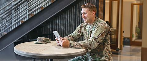 A government employee in camouflage uniform smiles while using a tablet