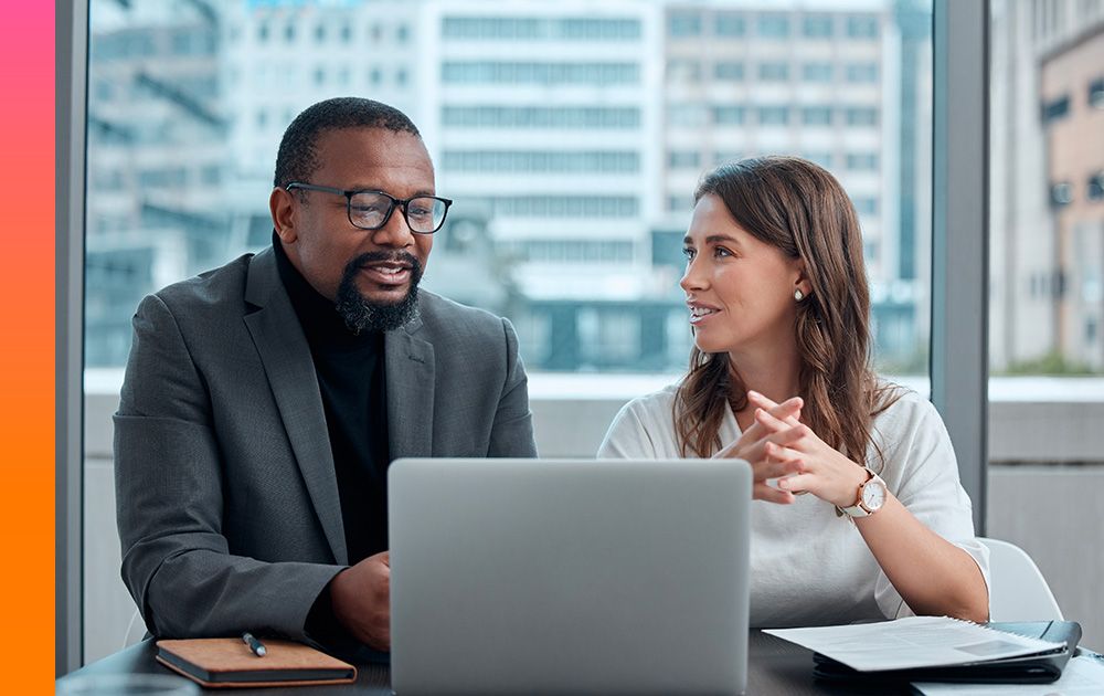 Two coworkers discuss their work sitting in front of a computer