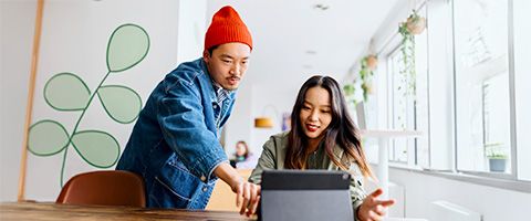 A couple of coworkers discuss their work on a tablet sitting on a desk