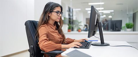 A woman in glasses working at a computer in a cubicle