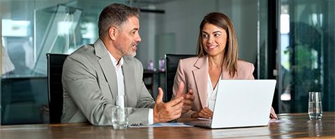 Two coworkers discuss their work at a computer in a conference room