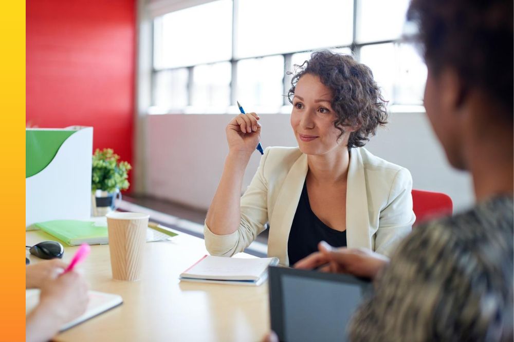Businessperson sitting and talking to two coworkers around a conference table