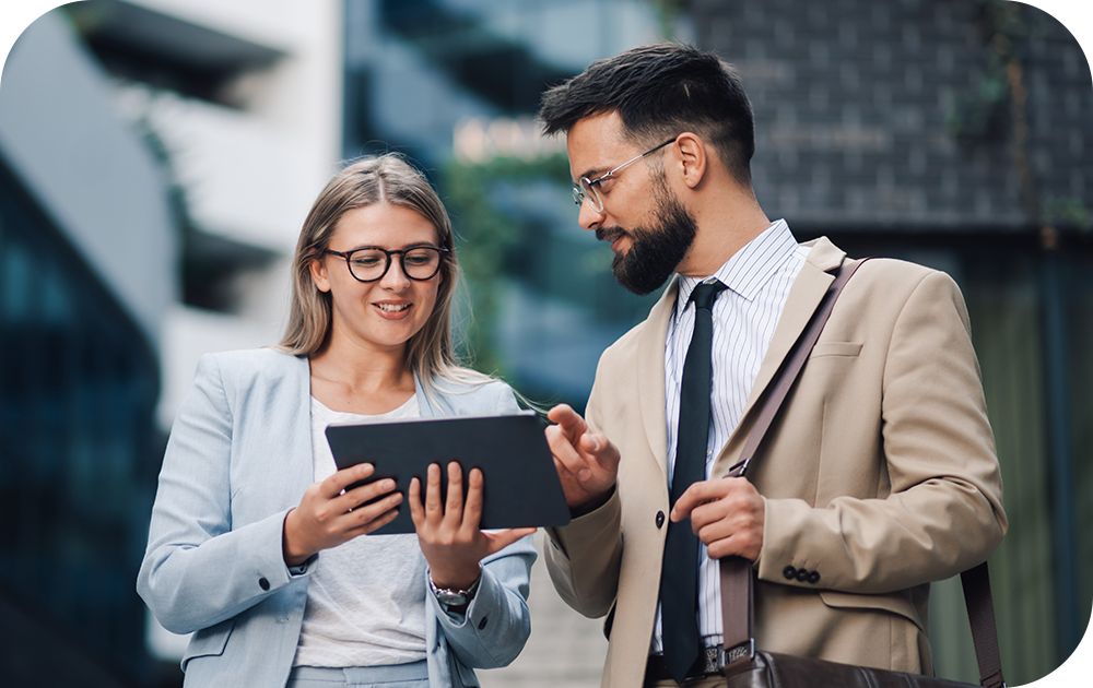Two businesspeople look at a tablet outside a building.