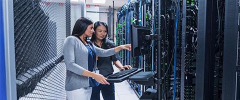 Two workers work at a computer at a server stack.