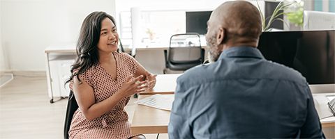 A man and woman have a discussion over an office desk. 