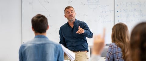 A man teaches a class in front of a whiteboard with math written on it