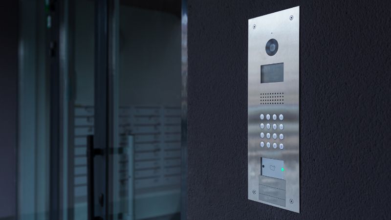 A silver security callbox is shown to the right of a closed glass door.