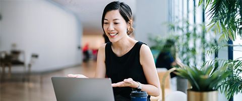 A person smiles and talks while looking at her laptop in a bright, spacious room.