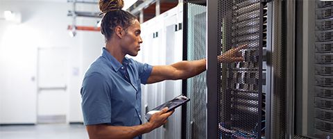 IT professional holding tablet device in hand while. checking server rack in data center. 