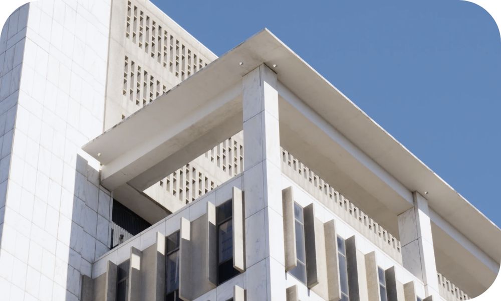 Close-up view of a modern concrete building featuring strong geometric lines, vertical fins, and an overhanging roof structure against a clear blue sky.