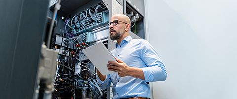 A person in a data center examines wiring with a tablet in hand.