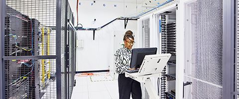 An individual stands and works at a large monitor in a data center.