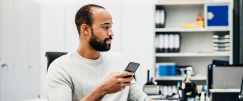 A person holds his phone up and focuses on the monitor in front of him.
