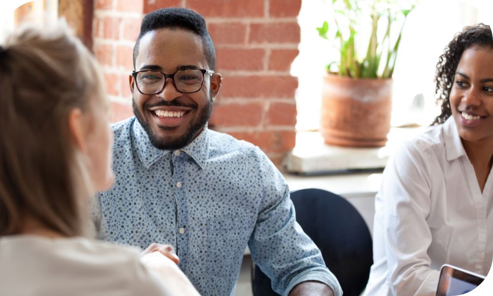 Three smiling people chat in an office setting.